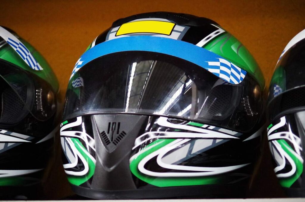 Trois casques de karting avec designs noirs, verts et bleus côte à côte