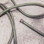 Tuyau vert enroulé sur béton, embout métallique détaché