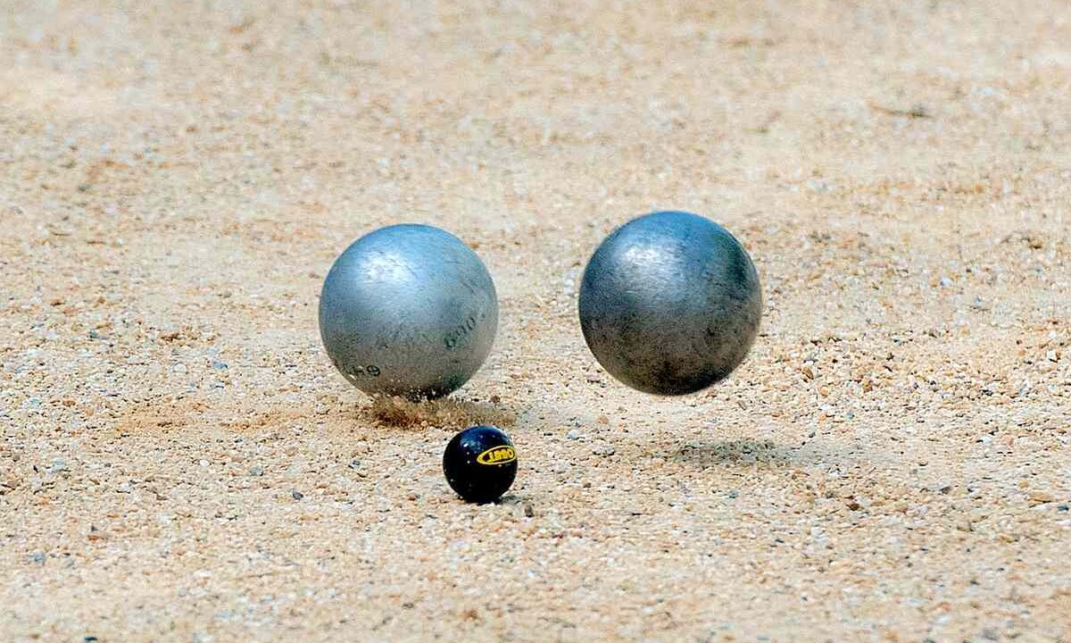 Deux boules métalliques et une petite balle noire reposent sur le sable