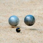 Deux boules métalliques et une petite balle noire reposent sur le sable