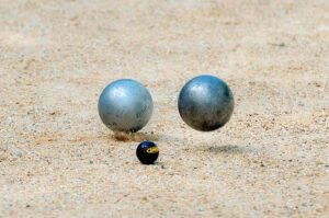Deux boules métalliques et une petite balle noire reposent sur le sable