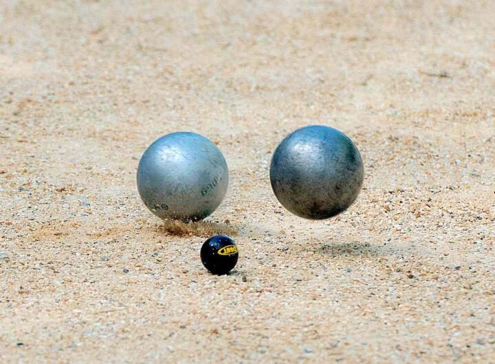 Deux boules métalliques et une petite balle noire reposent sur le sable