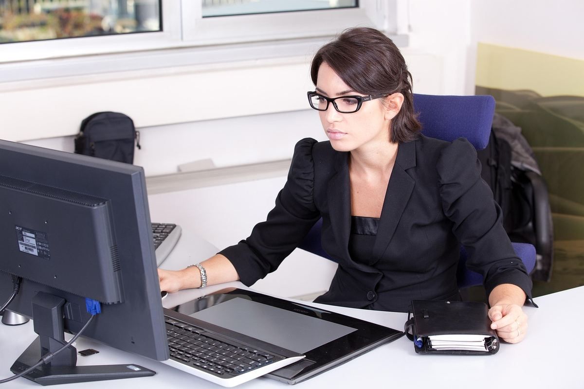 Une femme en costume noir travaille sur son ordinateur de bureau Une femme en costume noir travaille sur son ordinateur de bureau
