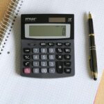 Une calculatrice posée sur un cahier quadrillé à côté d'un stylo