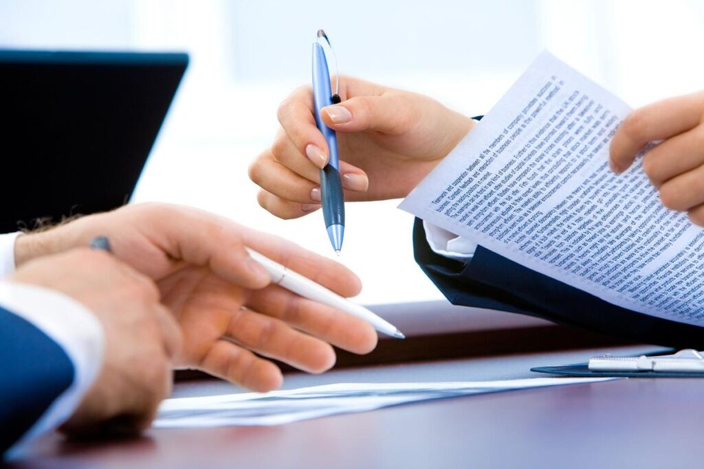 Deux mains échangent un stylo et des papiers sur un bureau