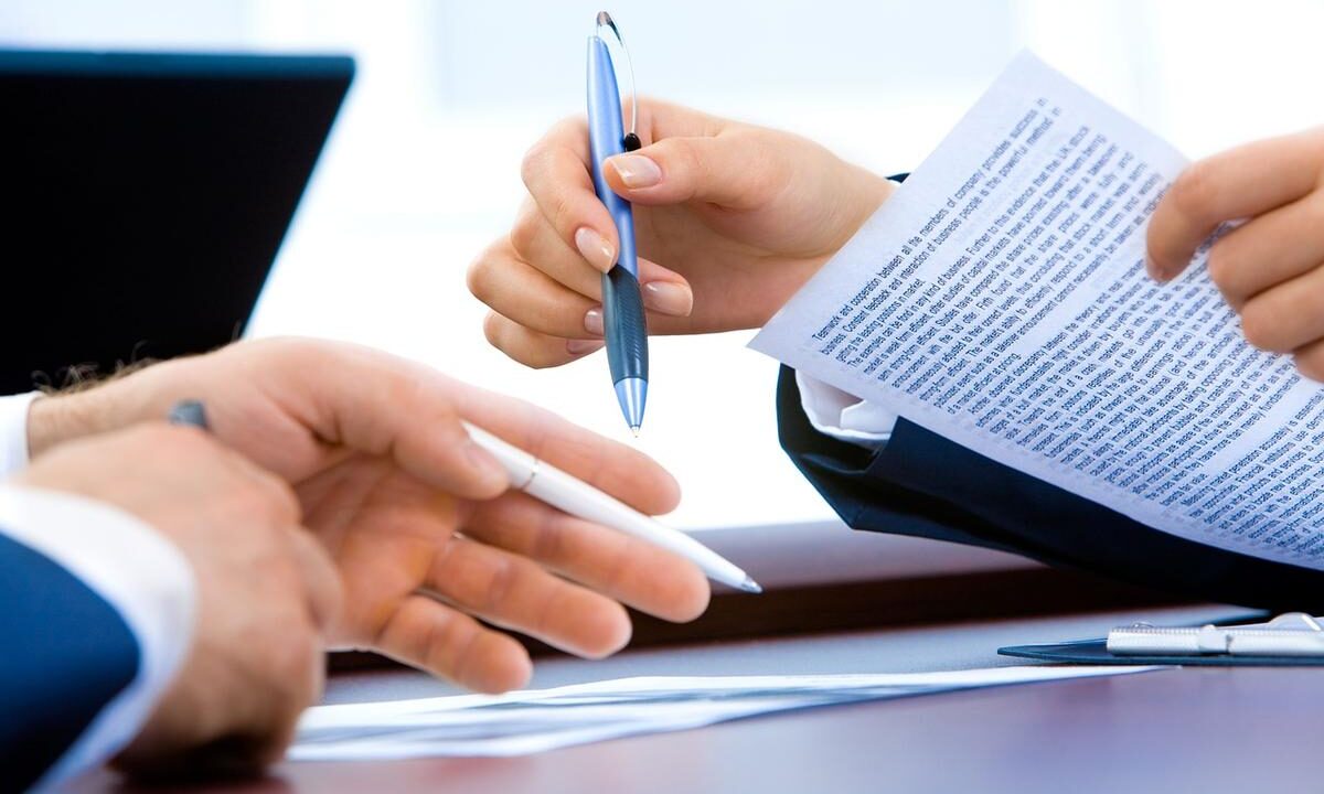 Deux mains échangent un stylo et des papiers sur un bureau