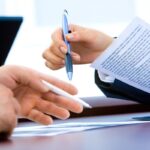 Deux mains échangent un stylo et des papiers sur un bureau